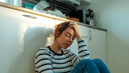Erschöpfte Frau, die auf dem Küchenboden sitzt und den Kopf mit der Hand abstützt