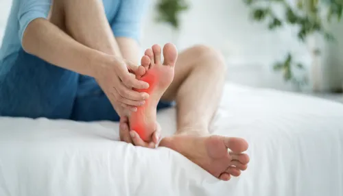 Älterer Mann, der sich auf dem Bett seinen schmerzenden Fuß fest hält