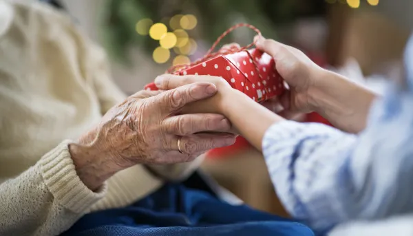 Nahaufnahme der Hände von einer älteren und einer jungen Frau, die zur Weihnachtszeit ein Geschenk halten.