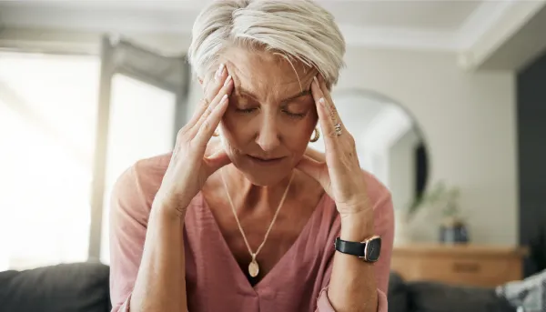 Ältere Frau mit Kopfschmerzen, Stress und Depressionen, während sie sich müde, ausgebrannt und ängstlich auf dem Sofa zu Hause fühlt.