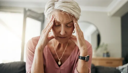 Ältere Frau mit Kopfschmerzen, Stress und Depressionen, während sie sich müde, ausgebrannt und ängstlich auf dem Sofa zu Hause fühlt.