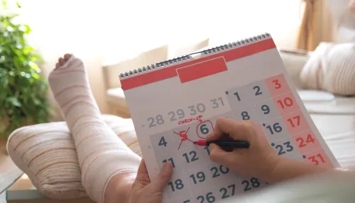 Eine Person mit einem bandagierten Fuß markiert einen Arzttermin im Kalender.