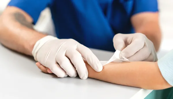 Pflegekraft in blauer Uniform bandagiert einen Arm.